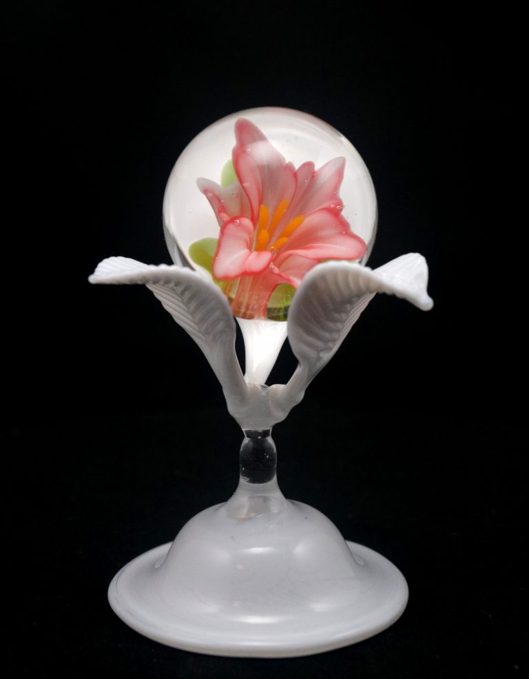 Marble with a pink lily inside, on a white glass flower-shaped stand