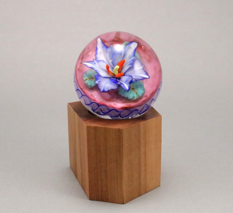 Marble with a blue and violet flower on a pink background, on a wooden stand