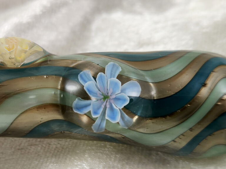 Close-up of a glass pipe: a light blue murrine flower on teal and amber stripes
