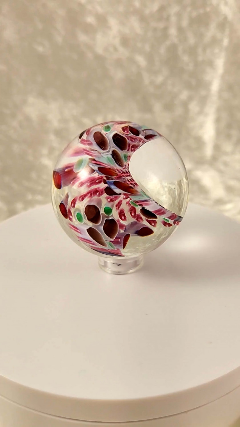 Clear marble with a curling band of red and pink glass on a white stand (video)